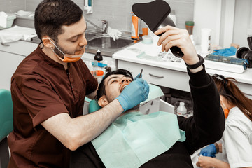 A young male dentist doctor treats a patient. Medical manipulations in dentistry, surgery. Professional uniform and equipment of a dentist. Healthcare Equipping a doctor’s workplace. Dentistry