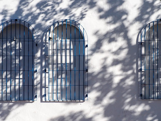 detalle de tres ventanas con arco sobre muro blanco y sombra de árbol