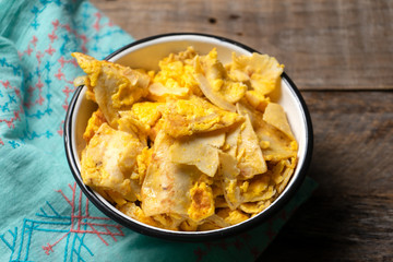 Mexican scrambled eggs with corn tortilla also called migas on wooden background