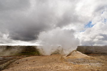 Vulkanlandschaft mit einer großen Fumarole, der viel Dampf entströmt, kontrastreicher Himmel mit...