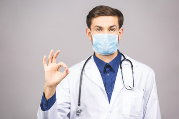 Portrait of young doctor in mask isolated on grey background. Ok sign.