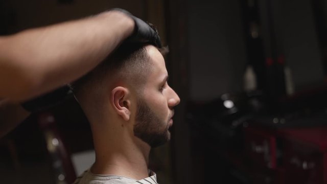 Professional barber doing hair styling for client with gel