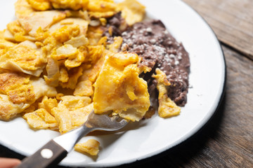 Mexican scrambled eggs with corn tortilla also called migas on wooden background