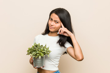 Young asian woman holding a plant showing a disappointment gesture with forefinger.