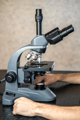 Male laboratory assistant examining biomaterial samples in a microscope. Cllose up hands in blue rubber gloves adjust microscope