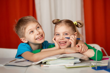 cute cheerful children of 8-9 years old, schoolchildren did homework at the table, a lot of textbooks are on the desk, children are happy looking at the camera in an embrace