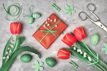 Easter flowers, eggs and gift boxes, flat lay on textured grey background. Red tulips, white baby...