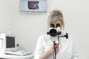 Fototapeta premium Female blond doctor gynecologist looks through a colposcope. Examination by a gynecologist. Female health concept
