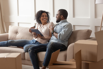 Smiling black family couple sitting on couch with tablet.