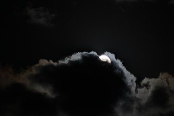Full moon rising in cloudy night sky