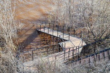 Stairs with wooden steps and iron railing going to the water on a Sunny day in early spring