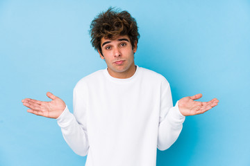 Young caucasian man against a blue background isolated doubting and shrugging shoulders in...