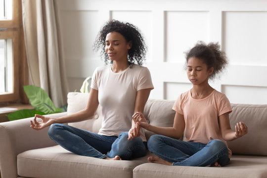 Black mother and daughter doing yoga exercises at home.