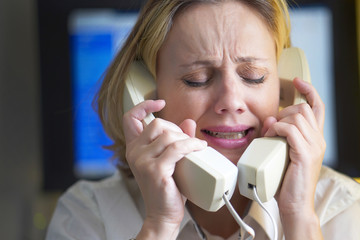 Face of office woman in stress with a lot of phone calls at same time. Unhappy woman holds two handsets of the phone. Busy office worker female working and answering a lot of calls at the same time.