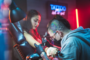 Young Woman Getting Tattoos In Beauty Parlor With Tattooist Working