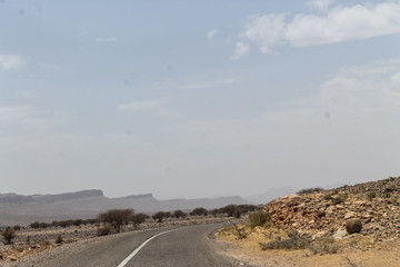 Empty road in southern Morocco with blue skies and mountains in the background