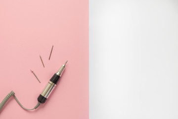 Electric nail drill manicure machine with different drill bits on pink and white geometric background