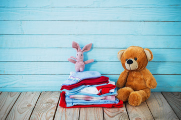 baby clothes and toy bear on old wooden background