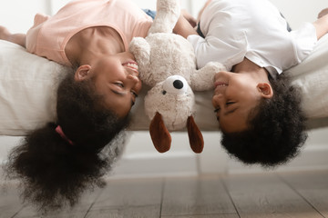 Happy black brother and sister laying upside down on bed.