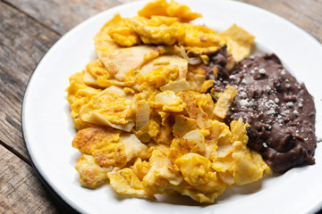 Mexican scrambled eggs with corn tortilla also called migas on wooden background