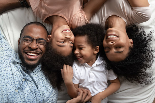 Smiling black family relaxing on bed with closed eyes.