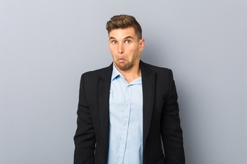 Young handsome caucasian man shrugs shoulders and open eyes confused.