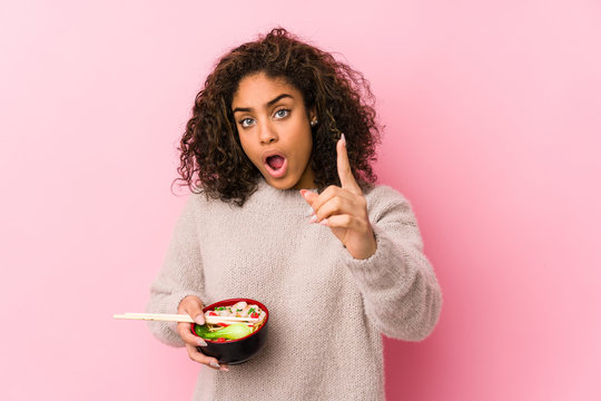 Young african american woman eating noodles having an idea, inspiration concept.