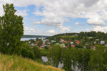 A scenic trail runs along the top of a hill above the Volga river. The path is surrounded by hedges and birches. Ples, Russia.