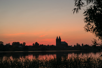Fototapeta na wymiar Two towers of the temple on a background of red, sunset sky. In the foreground is a reflection in the lake.