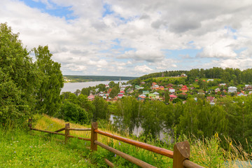 A scenic trail runs along the top of a hill above the Volga river. The path is surrounded by hedges and birches. Ples, Russia.