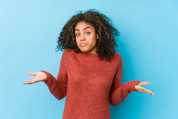 Young african american curly hair woman doubting and shrugging shoulders in questioning gesture.