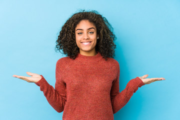 Young african american curly hair woman makes scale with arms, feels happy and confident.