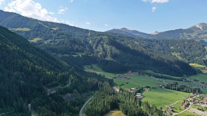 Fototapeta premium Aerial view of Tirol village in mountains near Krimml waterfall, Salzburg land, Austria. Houses, winding road, fir trees, blue sky, mountains.