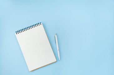 Empty spiral notebook with white pen on a blue background. Fashionable color and style. The apartment was lying. Copy space. The idea of a blogger.