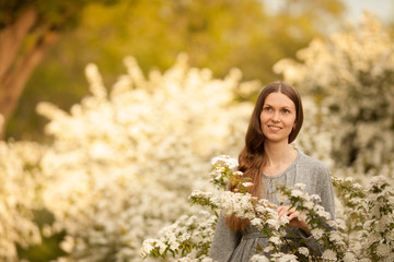 Beautiful girl in grey dress in spring in a blooming garden of white flowers. Place for the inscription. Concept: spring. March 8. Mother's day