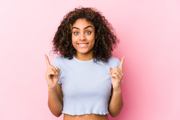 Young african american woman against a pink background indicates with both fore fingers up showing...