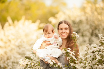 Beautiful young, happy woman with a baby in the spring in a blooming garden, smiling. Beautiful close-up portrait. Concept: spring. Mother's day. Natural beauty.