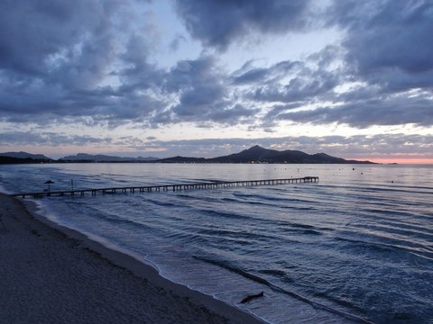 stuning view of the beach of Playa de Muro  in Mallorca at sunset with a pier, blue cloudy sky and a quiet sea with small waves.