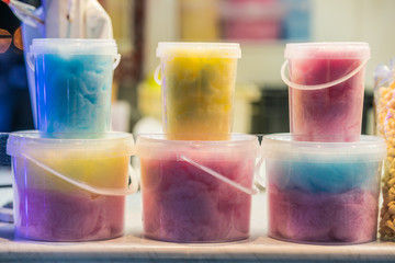 buckets filled with cotton candy of different colors in amusement park at night. The colors are...