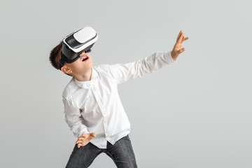 Little boy with virtual reality glasses on grey background