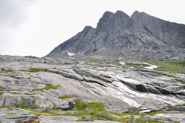 View to hiking trail to Tvillingene peak going upwards a grey stone mountain slope covered by grass and moss in the mountain range of Seven Sisters 