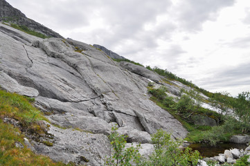 View to hiking trail to Tvillingene peak going upwards a grey stone mountain slope covered by grass and moss in the mountain range of Seven Sisters 