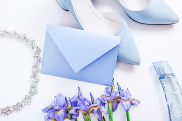 Wedding invitation surrounded with flowers, bride's shoes, perfume and jewellery. Morning of bride in blue color