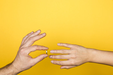 close up of man hand putting an engagement ring on a woman hand on yellow background