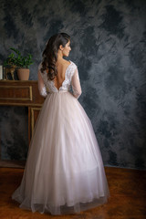 Fototapeta na wymiar Beautiful young woman stands in a delicate wedding dress against a dark wall