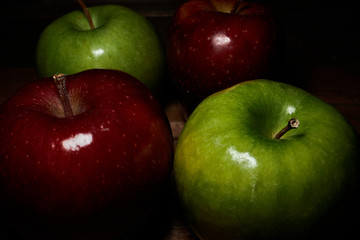 Four two red and two green apples on wooden table and dark background