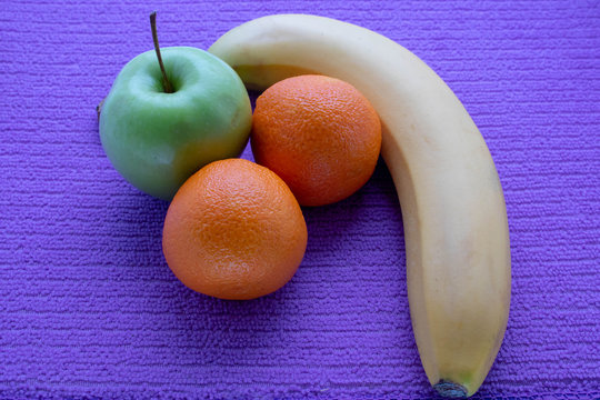 ffruit on a lilac napkin of resh mandarins and green apple and bananas on view from above