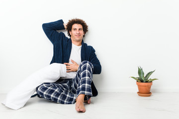 Mature man wearing pajama sitting on house floor stretching arms, relaxed position.