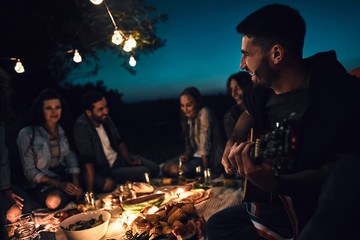 Man playing a guitar to his friends while camping.