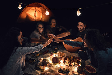 Group of friends giving high five while sitting around picnic place